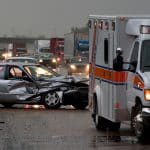Wallace-Law-Services-01 Totaled car on highway with ambulance nearby.
