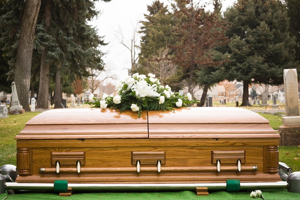 Casket in cemetery with white flowers on top